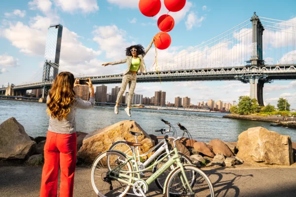 naine pildistab õhupallidega lendu tõusvat naist jalgrataste kõrval taustal suur sild